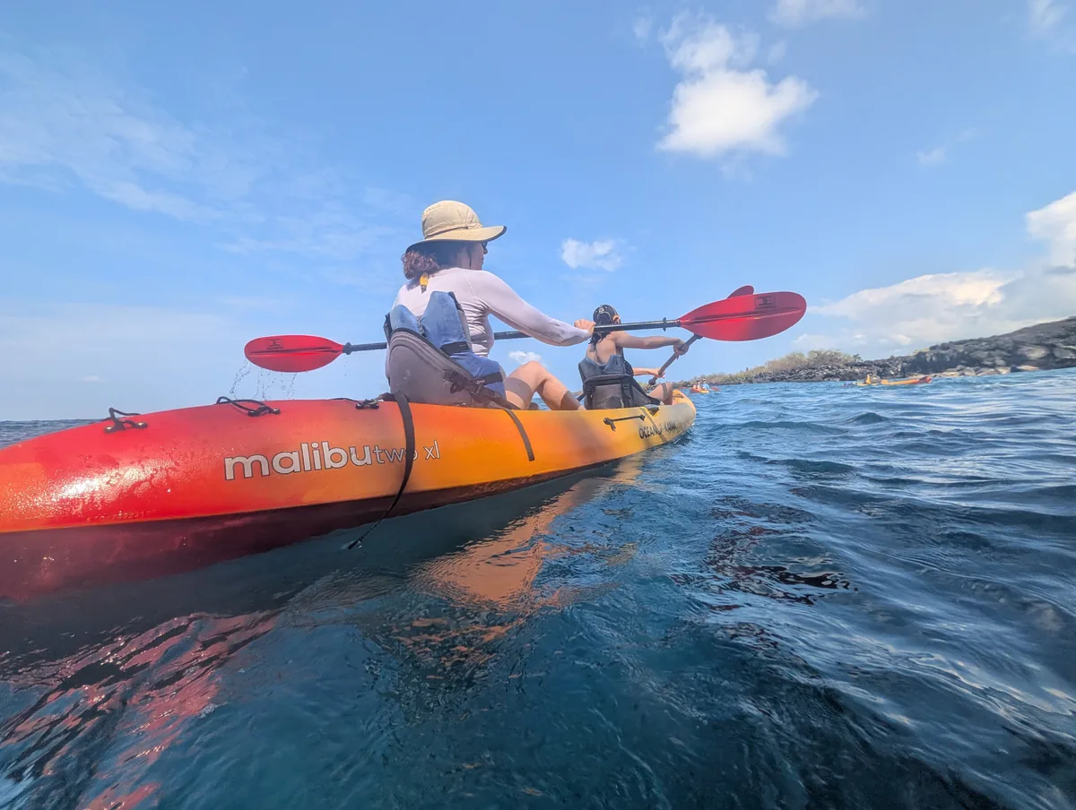 Guests in life jackets paddling one of our new red Malibu Two XL kayaks along the Kona coast