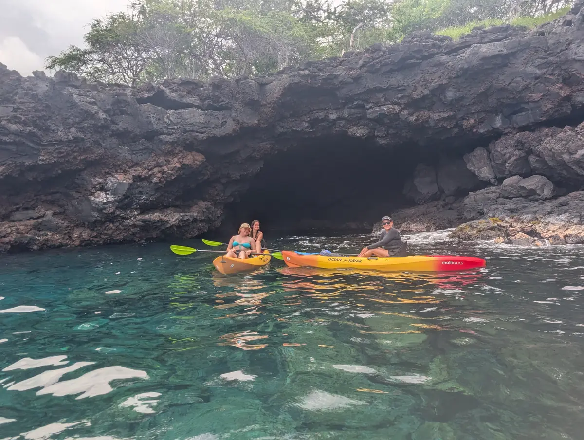 Kayakers at the mouth of the lava sea cave over glassy clear water